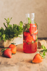 Homemade strawberry lemonade with fresh mint, rustic wooden table. Glass of refreshing summer natural drink, sunny light. Detox vitamin water. Copy space, vintage style photography.