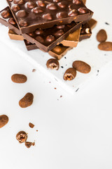 Stack of milk and dark chocolate with hazelnuts and macadamia nuts and dragee candies on white background.