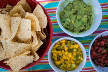 Tortilla Chips, Guacamole, and Mango Salsa in Bowls on a Picnic Table from Overhead.