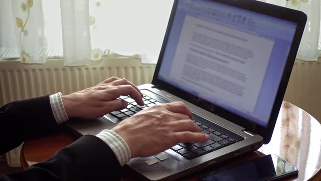 Closeup University professor working from home writing an essay using his laptop