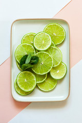 Lime slices with green mint leaves on dich on two colors paper background
