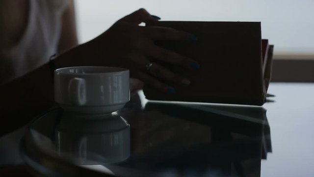 close up hands of young beautiful girl sits in a cafe with panoramic view. Morning with a cup of coffe, tea, book, notepad, reading, wrighting, drinking, communicate, use smrt phone