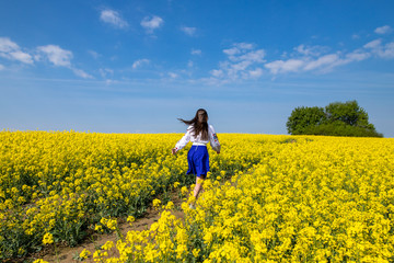 young woman running in a field with yellow flowers, blue sky, space