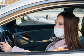 A young girl sits behind the wheel in the car in the mask during the global pandemic and coronavirus. Quarantine