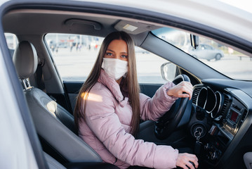 A young girl sits behind the wheel in the car in the mask during the global pandemic and coronavirus. Quarantine