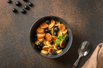 Homemade tiny pancake with blueberry on brown background. View from above. Trendy tasty breakfast.