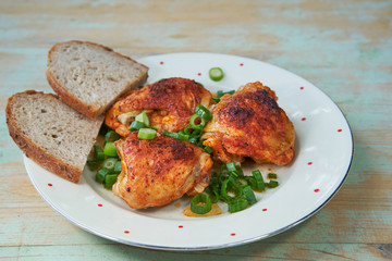 Top view on roasted hot spicy chicken leg pieces sprinkled with chopped spring onion and two slices of rustic bread. Served on the vintage porcelain plate. Tasty and juicy delicious light dietary dish