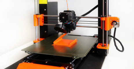 3D Printer in operation with orange filament on a white background