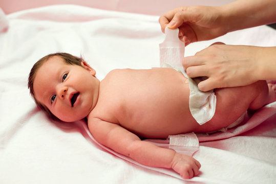 Mother putting on diaper on two weeks old child. Infant baby girl lying on back with open mouth while mom is changing her nappy. Closeup image. Hygiene and parental care concept