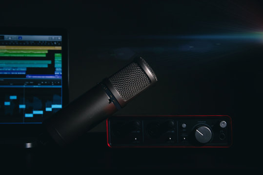 Audio recording basic set-up with a professional condenser microphone, audio interface and a editing software.
Black background with a light blur.
