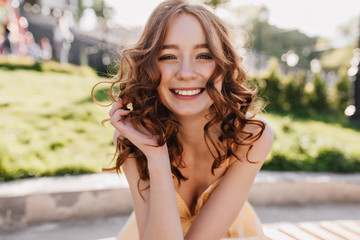 Dreamy red-haired girl posing with sincere smile on nature background. Gorgeous ginger curly woman enjoying sunny summer morning.