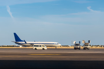 International airlines plane parking outside a terminal in airport. White passenger airplane, side view. Airfield cars, trucks and equipment, aircraft preparation before flight.