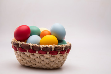 Naklejka na ściany i meble Multicolored Easter eggs in a basket on white background.