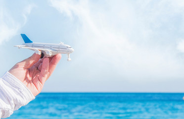 Man hand holding airplane model over sea background dreams of journey in vacation.