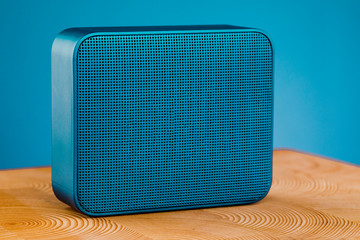 Portable blue wireless speaker, on a wooden table on a blue background.