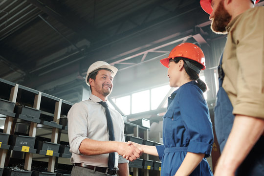 Positive handsome businessman in hardhat handshaking with factory engineer in contemporary shop of industrial plant
