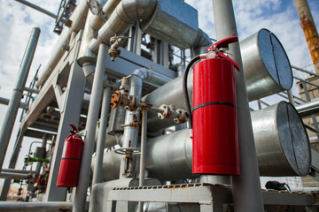Close-up of red fire extinguisher on oil refinery plant. Grey pipes and pipe-lines and blue sky...