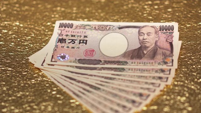 Close-up slide video of 100,000 yen in cash sent by the Japanese govt of Abe Shinzo to fight economic unemployment crisis caused by COVID-19 on a golden background.