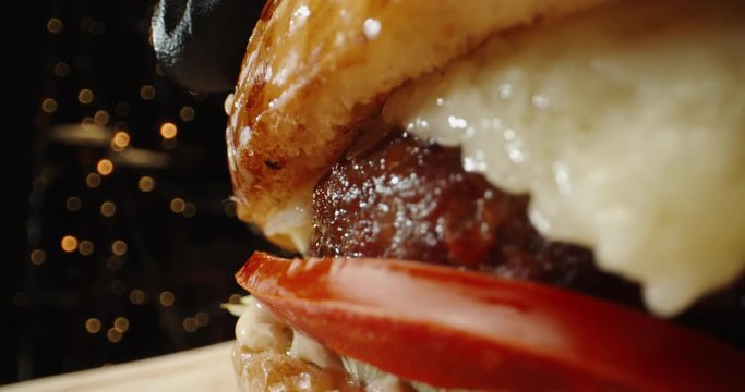 Close up shot of large tasy burger with beef steak, iceberg cabbage, tomatoes, pickles and melted cheese, rotating - fast food, food preparation 4k footage