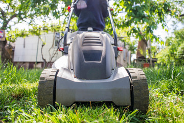 Man is mowing the lawn. Man with lawnmower is mowing green grass in the garden. Gardening