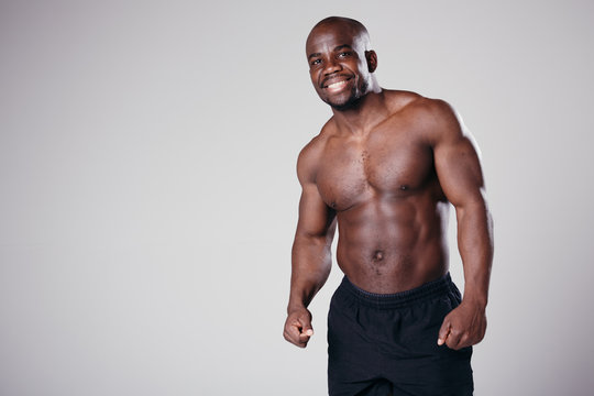 Portrait of a dark-skinned Pilates trainer with a naked torso in black shorts posing in front of the camera on a light background