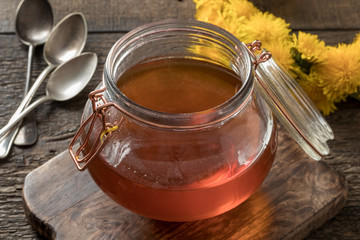 A jar of dandelion honey with fresh dandelion flowers