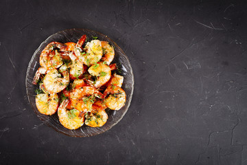 Fried shrimp with dill lie in a plate on a dark table, top view, place for your menu text