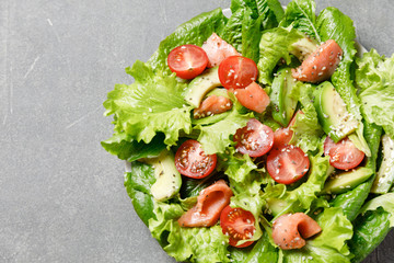 Salmon salad with avocado, green leaves, tomatoes on gray background