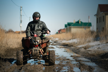 Biker is sitting on the quad bike on dirty country road.