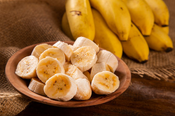 Naklejka na ściany i meble A banch of bananas and a sliced banana on wood background.