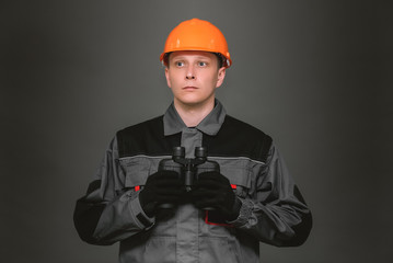 A construction worker in hardhat with binoculars in hands on gray background.