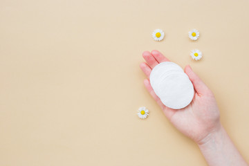 Cotton pads on woman hand and fresh chamomile on a beige background. Flat lay, top view, copy space. Women's health care