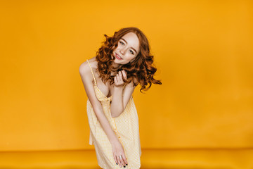 Fascinating white girl with ginger hair dancing in studio. Lovable female model with wavy hairstyle posing with smile on orange background.