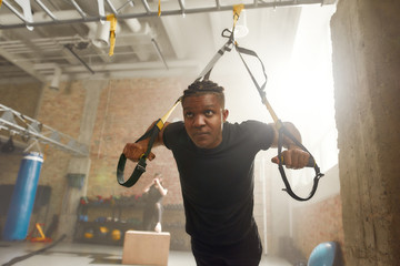 Athletic young man doing fitness TRX training exercises at industrial gym. Push-up, group workout...