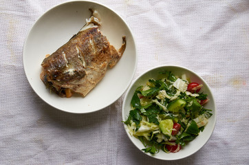 Piece of fish in a white plate and green salad