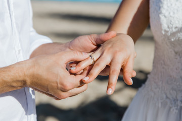 Bride and groom exchanging wedding rings close up during symbolic nautical decor destination wedding marriage on sandy beach in front of the ocean in Punta Cana, Dominican republic 