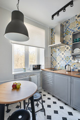 A minimalistic, compact kitchen with grey facades, Moroccan tiles and an open hanging Cabinet with plates, glasses and containers for storing food
