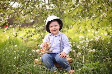 Little cute blond boy playing with a wooden plane in the summer park on the grass on a sunny day, focus on the child, blurred background