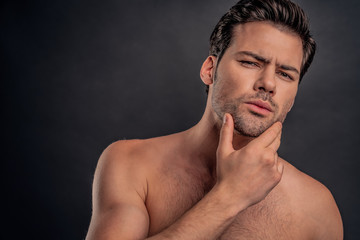 Fototapeta premium Handsome man. Charming young naked man keeping hand on chin and while standing against grey background