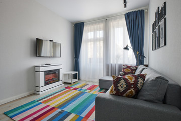 Minsk, Belarus, may 2020: Scandinavian-style living room with sofa, colored carpet, wooden bed, Electric fireplace and vintage lamps