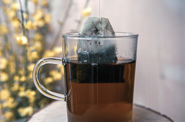 close-up of glass with hot tea and teabag and yellow flowers