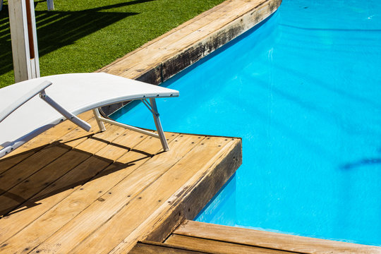 summer relaxation vacation time swimming pool site deck chair furniture white lounge object under bright sun lighting near blue water space