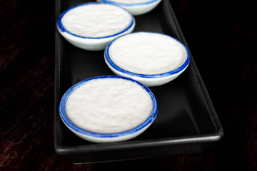 Coconut Milk pudding or Khanom Thuai in black tray on wooden table.