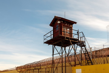 Fototapeta na wymiar Prison tower and barbed wire fence. Wooden tower with room for guard of prisoners in pre-trial detention center or prison zone