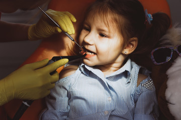 High angle of crop dentist in gloves using professional tools to check teeth of little patient