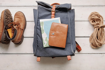 Above view of hiking backpack with map and purse placed on wooden floor with boots and rope