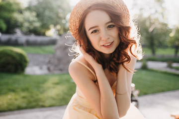 Good-looking ginger girl in hat posing on blur nature background. Refined caucasian lady with red wavy hair chilling in park.