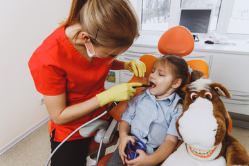 High angle of woman in dentist uniform checking teeth of little girl near plush horse while working in contemporary clinic