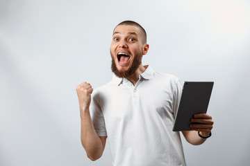 Portrait of a handsome happy bearded man in a white T-shirt with a tablet on a white background. isolated, emotions