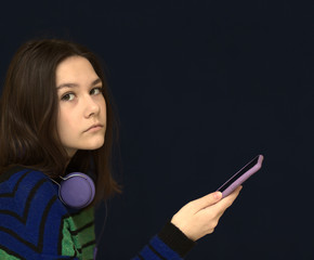 Contented smiling girl typing text message or scrolling through social networks using smartphone. Dark background